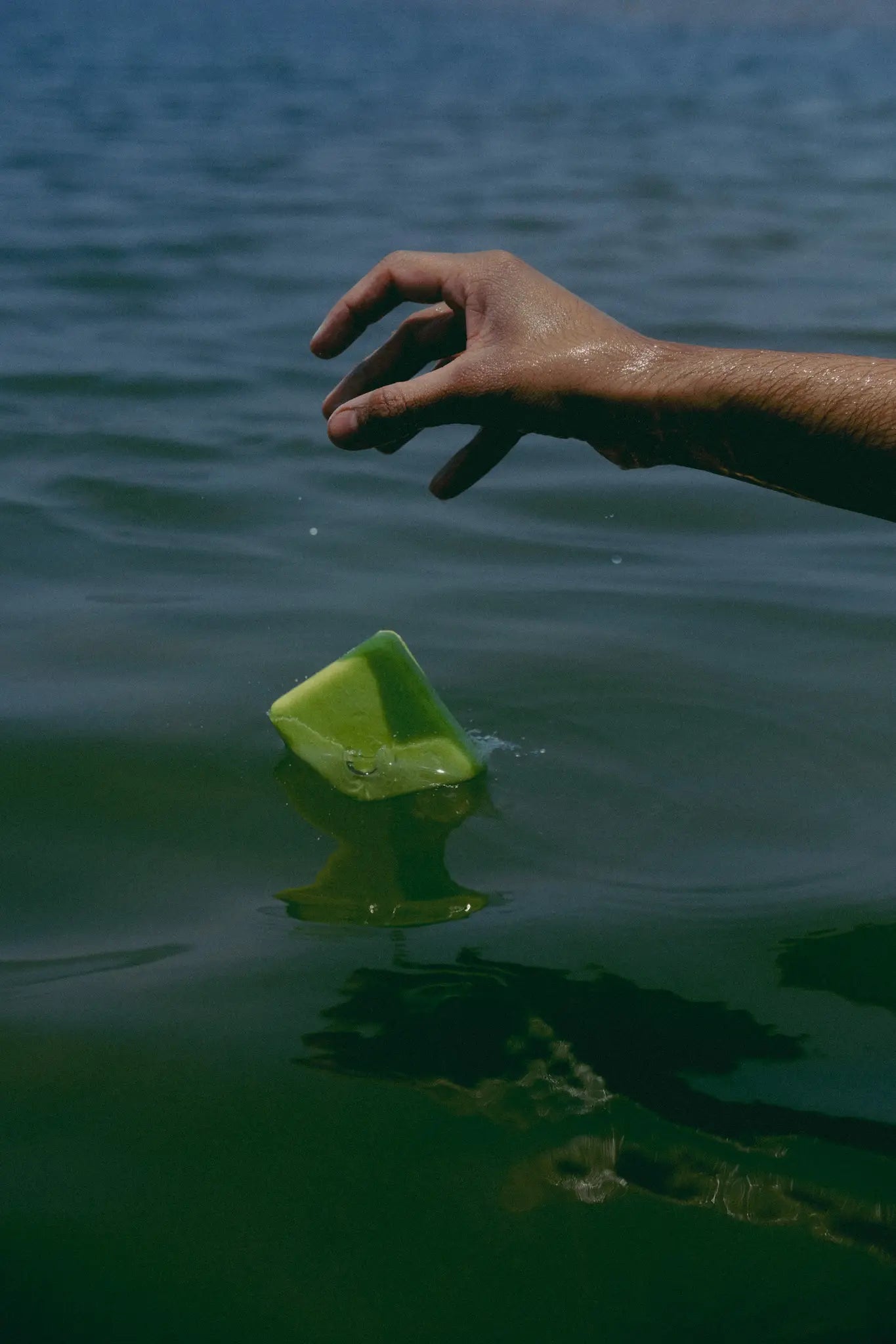 Hand reaching towards a green natural cold process soap floating on water
